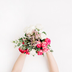 Woman hands holding wedding bouquet with white, pink and red roses, eucalyptus branch, wildflowers on white background. Flat lay, top view festive wedding concept.