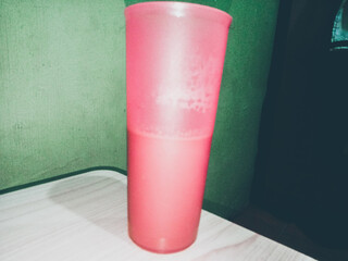 A close-up view of a pink plastic cup from the side. Inside is a quarter of brown milk. The cup is sitting on a table.