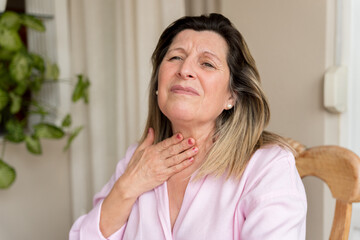 An older woman touching her throat, possibly suffering from hoarseness and experiencing pain and...
