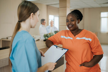 Fototapeta premium Nurse reviewing patient record in hospital hallway. Two healthcare professionals discussing medical records on a clipboard in hospital, collaborating on patient care