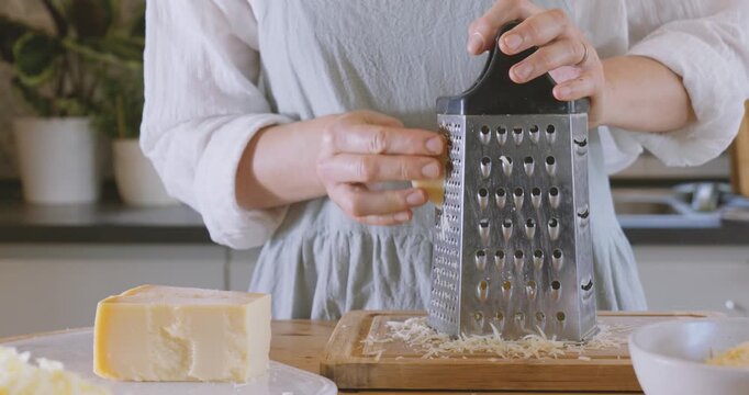 Woman prepares ingredients for eggplant parmigiana, grating parmesan cheese on cutter board