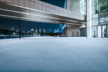 Empty stone ground of an outdoor plaza in front of a modern office building with the city skyline at night. © zhao dongfang