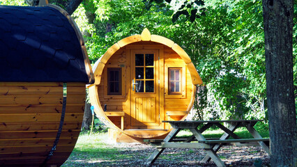 Glamping and unusual architecture: a comfortable wooden barrel-shaped house (sleeping barrel) immersed in the greenery of a campsite

