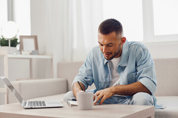 Focused man enjoying a morning routine, sipping coffee, and working on a laptop at home in a bright, cozy environment with natural light.