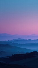 Fototapeta premium Dreamy, hazy twilight landscape of rolling hills and valleys bathed in soft pink and blue hues, creating a serene and ethereal atmosphere. The image features a soft focus and muted color palette