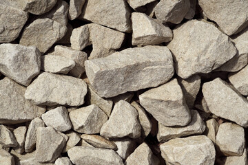 Various sizes of light-colored gravel stones pile up in an outdoor setting under bright natural light