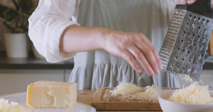 Woman prepares ingredients for eggplant parmigiana, grating parmesan cheese on cutter board