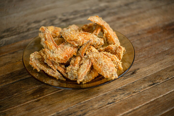 
A pile of crispy, golden-brown fried chicken wings on a glass plate, resting on a rustic wooden table, perfect for snacks or appetizers