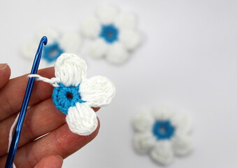 A flower with six white petals and a blue center crocheted on a white background.
