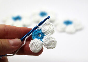 A flower with six white petals and a blue center crocheted on a white background.