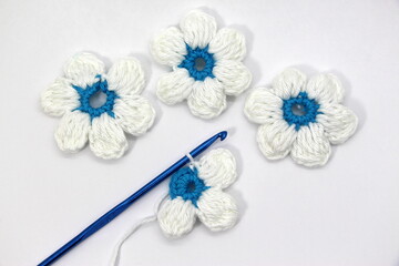 A flower with six white petals and a blue center crocheted on a white background.