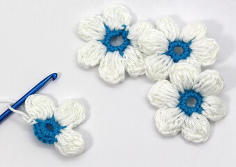 A flower with six white petals and a blue center crocheted on a white background.