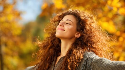 Naklejka premium A young woman stands with her arms wide open basking in the warmth of the sun on a beautiful day. Vibrant autumn leaves create a stunning backdrop enhancing her joyful expression.