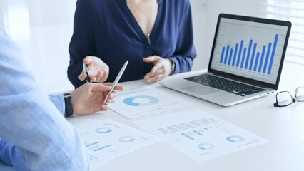 Business professionals collaborating on a laptop, reviewing financial documents, and discussing project strategies in a modern office. Businesspeople in finance concept