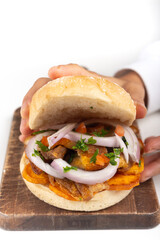 Hands presenting bread with chicharrón, a typical Peruvian dish.