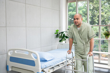 A patient in recovery struggles to walk with a walker, showing determination and pain as he takes small steps beside his hospital bed in a bright, peaceful room.