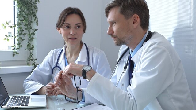 Two doctors are studying medical charts on a laptop, discussing patient data in a hospital or clinical setting. Medicine and healthcare concept.