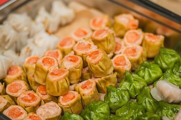 Colorful assortment of dim sum dishes featuring shrimp dumplings, pork siu mai, and vibrant green dumplings arranged neatly in a metal tray, showcasing culinary artistry and tradition