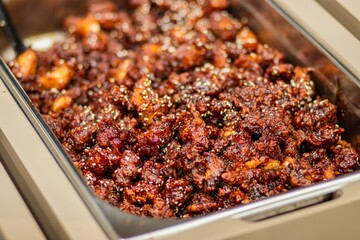 Deliciously cooked spicy chicken dish served in a stainless steel tray, garnished with sesame seeds, showcasing vibrant colors and rich textures, perfect for culinary presentations