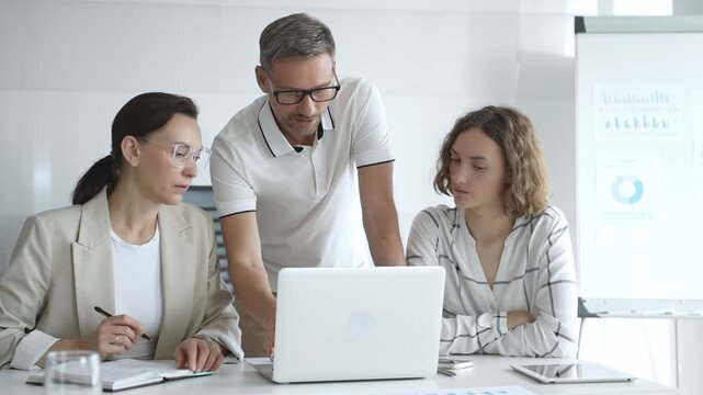 Business team collaborating and analyzing data on a laptop during a dynamic office meeting, uniting efforts to reach shared objectives and drive successful outcomes together
