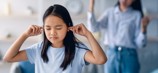 Family argument concept. Offended asian girl covering ears, not wanting to listen to her mother's...