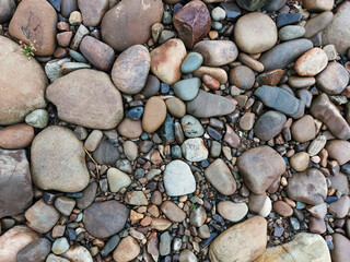 Close-up of smooth river stones and pebbles in natural earthy tones. Background texture of polished rocks.
