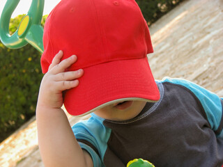 Toddler wearing a big red cap outdoors, playful childhood moment