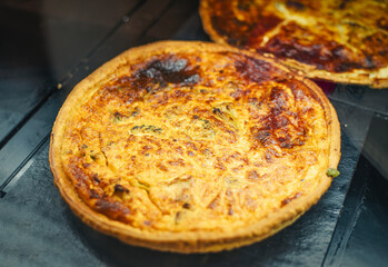 A freshly baked quiche with a golden, crispy crust is showcased. The quiche features a filling of herbs and vegetables with a slightly charred top.