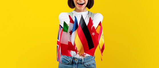 Foreign language studying school concept. Excited lady showing bunch of diverse flags, posing and smiling to camera over yellow studio background, free space © Prostock-studio