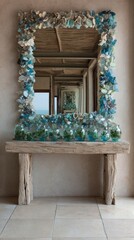A large, decorative mirror, framed with a mosaic of various shades of blue, grey, and white glass pebbles, sits atop a rustic, wooden console table.