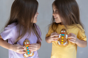 Twin sisters hold gingerbread man cookies in hands looking at each other and smiling. Close up...