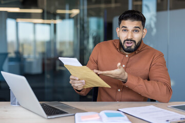 Young businessman sitting at desk in office receiving surprising news while opening an important...