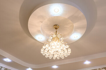 Elaborate ceiling with a tiered design and a crystal chandelier. Spotlights illuminate the recessed tiers
