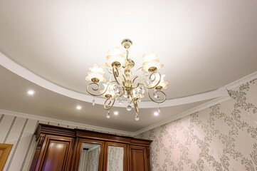 Elegant room featuring a gold chandelier with crystal drops, decorative wallpaper, and a dark wood...