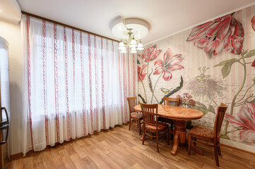 Cozy dining room boasts floral wallpaper, a wood table with patterned chairs, and sheer curtains filtering natural light
