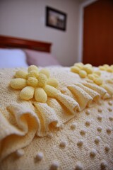 Delicate, yellow crocheted flowers adorn a light beige knitted blanket with ruffles, creating a cozy and inviting bedroom scene.