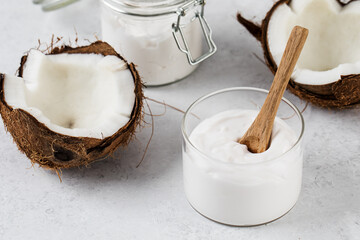Fresh coconut yogurt in a glass jar with a wooden spoon and coconuts. Vegan yogurt, lactose-free.