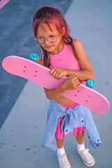 A stylish girl stands with a skateboard in hands in a skate park. Skate riding skills. Active sports hobbies