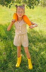 A funny girl in rubber boots holds two large yellow squash in the garden. Harvest season