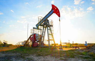 Oil Pump Jack Operates on Beautiful Sunset at Oil Field in Industrial Area. Crude pump jack working on sunrise in oil field. Oil drill rig, drilling derrick in oilfield. Crude petroleum industry.