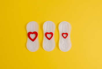 Women's sanitary pad with red hearts on a yellow background.