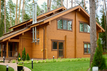 Contemporary wooden house with sloped roof nestled among tall trees. Warm brown tones complement lush greenery, creating serene forest atmosphere. Natural light enhances cozy feel