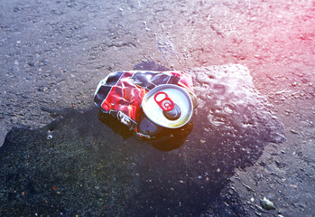 Canned drink spilled on asphalt road on sunset landscape in serene outdoor setting. Beer can lies on wet asphalt. Spilled drink from crumpled Beer Can. Discarded broken drink tin can on asphalt road