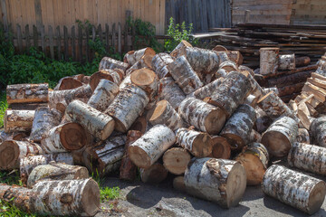Pile of logs with some of them being cut in half. The pile is in a yard and is surrounded by grass