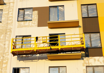 Suspended construction cradle on painting facade of building. Mobile scaffolding platform for construction work at height, facade cleaning, plastering. Insulation and wall painting, cladding.