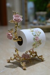 Ornate gold-toned paper towel holder featuring delicate pink roses and floral designs, showcasing a refined and elegant aesthetic.