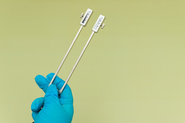Blue Gloved Hands Holding tuning fork On green Background, medical instruments in the hands of a...