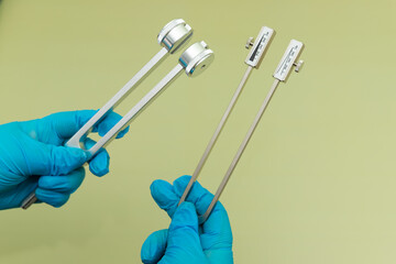 Blue Gloved Hands Holding tuning fork On green Background, medical instruments in the hands of a...