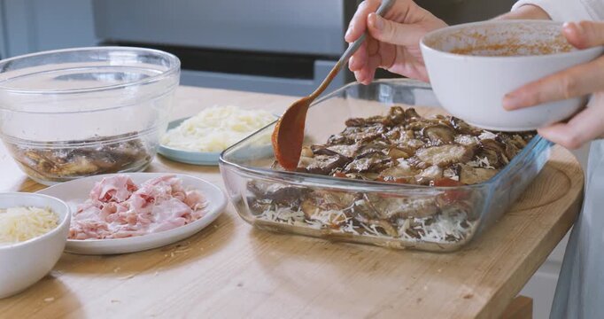 Woman prepares eggplant parmigiana, putting tomato sauce on fried slices of eggplant into lasagna pan