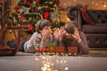two boys are having fun playing with a train under a Christmas tree